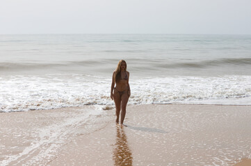 beautiful young blonde woman coming out of the sea is walking along the shore of the beach. The woman is wearing a leopard bikini and enjoying her summer holidays in spain.
