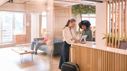 Businesswoman With Suitcase Checking In At Hotel Reception For Conference
