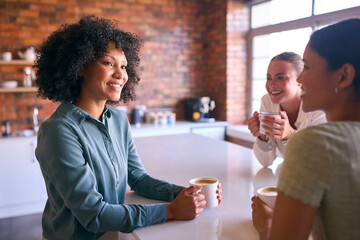 Multi-Cultural Businesswomen Taking Coffee Break In Kitchen Area Of Modern Open Plan Office Together