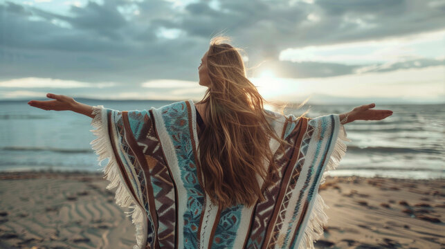 Back view of a young woman wearing colorful poncho relaxing in beautiful nature with opened arms. Spirituality, harmony and connection with nature concept.