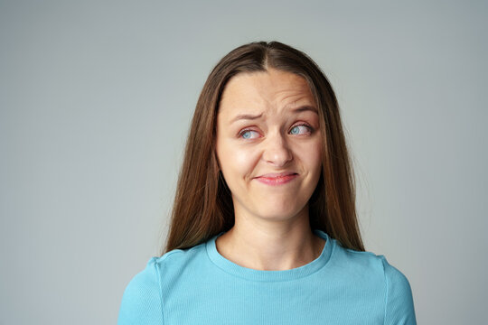 Disgusted and frowning young woman on gray background