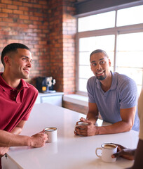 Multi-Cultural Businessmen Taking Coffee Break In Kitchen Area Of Modern Open Plan Office Together