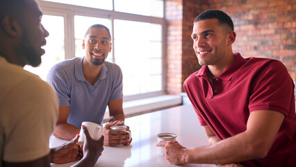 Multi-Cultural Businessmen Taking Coffee Break In Kitchen Area Of Modern Open Plan Office Together