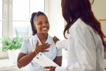 Black woman doctor or nurse is talking with a happy patient in a hospital. The atmosphere is one of genuine care, with the medical professional engaging in a conversation. - obrazy, fototapety, plakaty