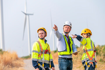 Engineer surveyor and manager wearing uniform walking holding box inspection and tablet work in wind turbine farms rotation to electricity, alternative renewable energy for clean power energy concept.