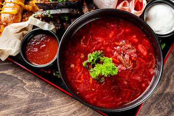 A vibrant bowl of red soup, garnished with herbs, sits atop a wooden surface. Grilled meat and...