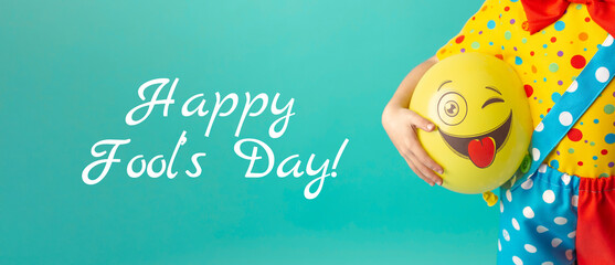 A bright yellow ball with a cheerful face in the hands of a clown child. Birthday and 1 April Fool's day concept