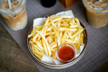 French fries in a bowl on a wooden table with glasses of ice coffee background at cafe or...