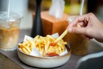 Close up hand of woman dipping French fries into red sauce in cafe.