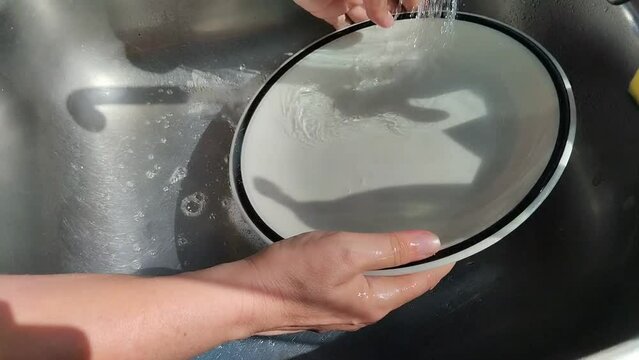 Unas manos de  mujer lavando un plato de color blanco  con  agua  en un fregadero