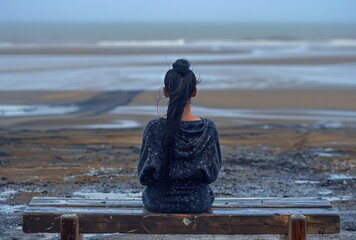 A woman with summer depression sitting on an empty bench overlooking the ocean, back view. 