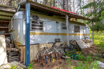 A rundown abandoned covered mobile home trailer in the rural forest with debris scattered nearby.