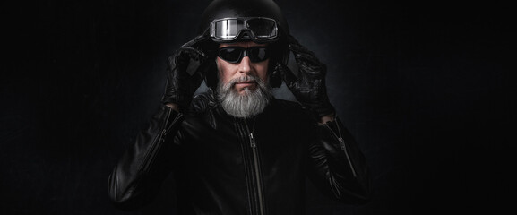 Portrait d'un motard homme avec un casque noir et une veste en cuir et des lunettes de soleil et une barbe grise vintage