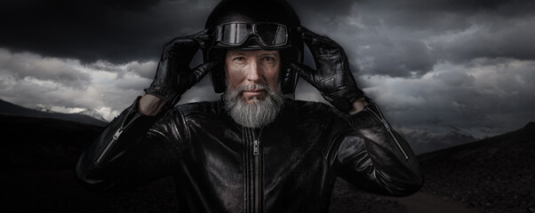 Portrait d'un motard biker homme avec un casque noir et une veste en cuir et une barbe grise vintage