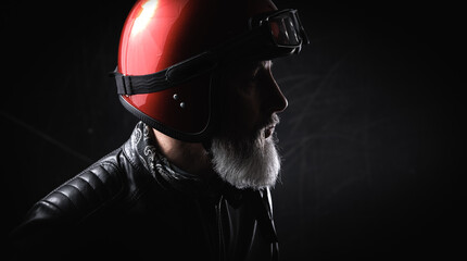 Portrait d'un motard homme avec un casque rouge et une veste en cuir  et une barbe grise vintage