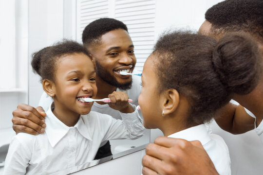 African-american girl brushing teeth together with dad