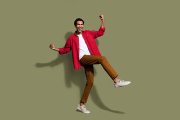 Fototapeta na wymiar Full length photo of crazy lucky guy wear red shirt screaming yeah rising fists empty space isolated khaki color background