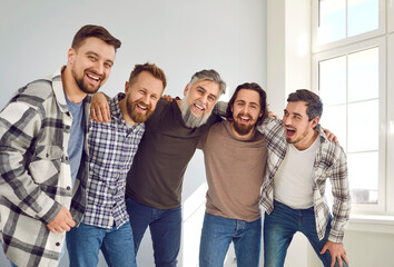 Happy huddling men. Group of cheerful male friends hugging and having fun together. Indoor shot of...
