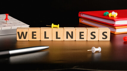 Wellness text on wooden cubes on a glossy black background next to office supplies