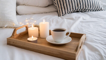 Fototapeta na wymiar Hygge concept Coffee and candle filled wooden tray on a bed accompanied by white bedding striped blanket and pillow serving breakfast