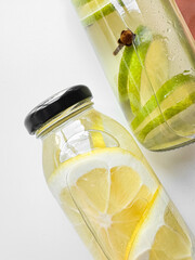 Close up of detox drinks lemon and lime in glass bottles on white background. Macro photography...