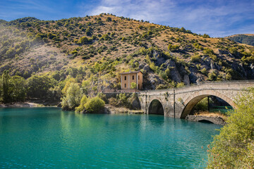 Fototapeta na wymiar Lake San Domenico, in the Sagittario Gorges, in Abruzzo, L'Aquila, Italy. The small hermitage with the stone bridge. The turquoise color of the water. The glow of the sun, flare at sunset.