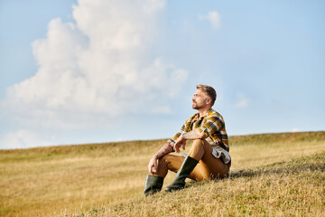Naklejka na ściany i meble good looking dedicated man with beard relaxing on green spring field and looking away, modern farmer