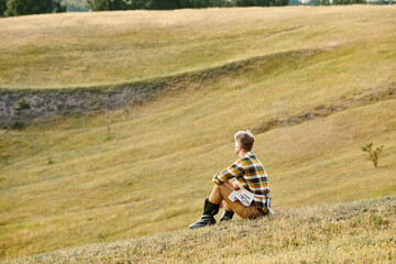 good looking dedicated man with beard relaxing on green spring field and looking away, modern farmer