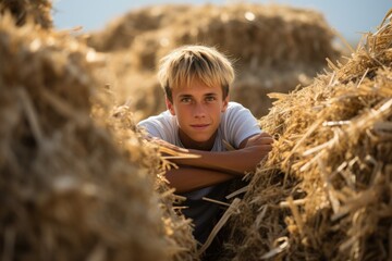 Naklejka na ściany i meble A young boy seated amidst a large pile of hay