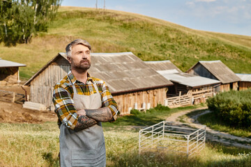 appealing dedicated modern farmer with tattoos and beard relaxing in his farm and looking away