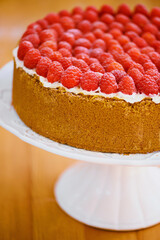 Stand, frosting and cheesecake with raspberries on table for sweet snack for tea time at home. Bakery, catering and closeup of gourmet dessert with crust, cream and fresh organic fruit in dining room