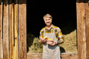 joyous handsome farmer with tattoos holding homemade cheese in his hands and smiling at camera - obrazy, fototapety, plakaty