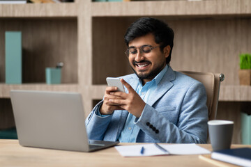Indian executive businessman communicating through smartphone seated in modern office