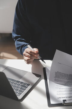 Asian businessman reviewing document reports at office workplace with computer laptop. legal expert, professional lawyer reading and checking financial documents or insurance contract