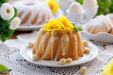 Traditional Easter cake, Babka covered with icing decorated with chocolate eggs and primrose flowers on a festive table, close up view