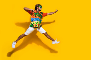 Fototapeta na wymiar Full size photo of active man dressed print shirt flying clenching fists look at discount empty space isolated on yellow color background