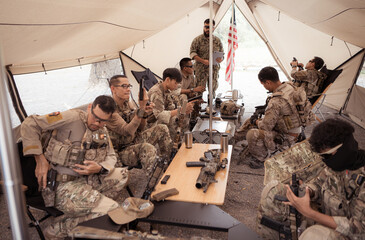 Group of soldiers in camouflage uniforms hold weapons in a field tent, Plan and prepare for combat...