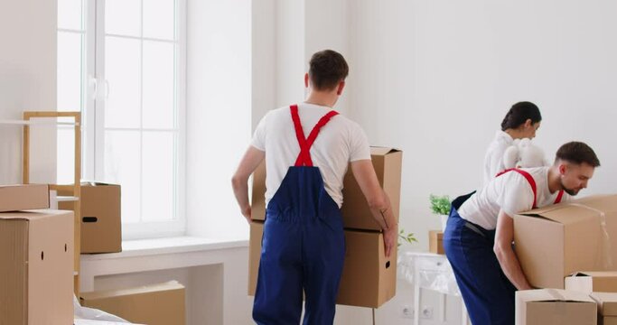 Men, movers staff from a relocation service, are helping a woman client carry cardboard boxes during a home or office relocation. Their smiling staff ensures a helpful and positive moving experience.