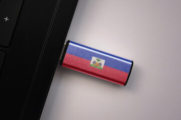usb flash drive in notebook computer with the national flag of haiti on gray background.
