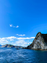 Majestic rocks are surrounded by the sea. The background is bright blue sky