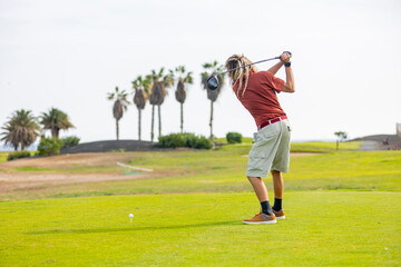 Trendy golfer with dreadlocks swinging on the course