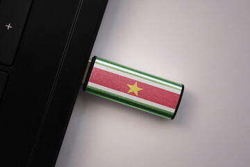usb flash drive in notebook computer with the national flag of suriname on gray background.