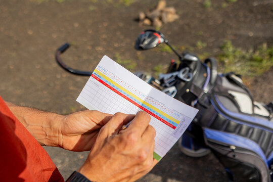 Golfer checking the scorecard with equipment in background