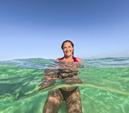Woman smiling in the ocean, split view above and underwater