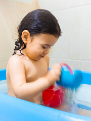 Hermosa niña blanca de dos años disfrutando su baño,  jugando con el agua en su bañera y...