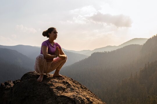 Captured at dusk, a yogi squats in a pose of reflection on a high rock, overlooking layers of mountain silhouettes