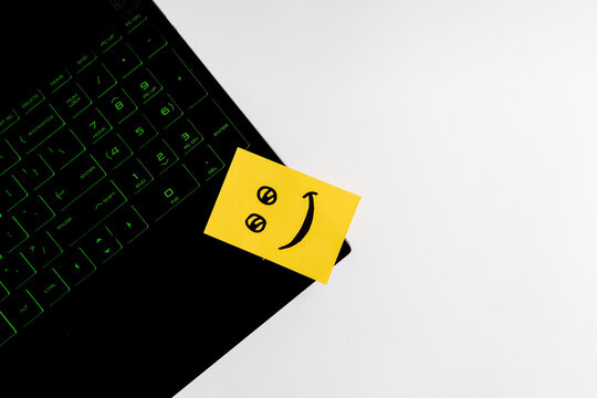 Top view of happy face sticky note on keyboard over wooden background.