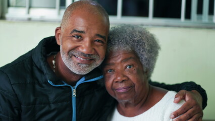 Adult African American 50s son posing with his elderly senior 80s mother, close-up faces smiling in...