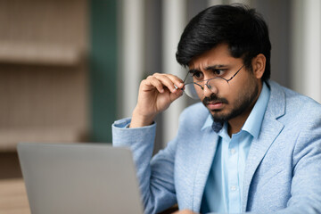 Indian man dealing with eyesight issues squints at laptop indoor