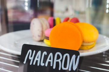 Macaroons on showcase in cafe. Macaron cake with price tag. Sweet food concept. Morning dessert. Orange macaron on plate in marketplace. Dessert assortment. French biscuit. - 757429769